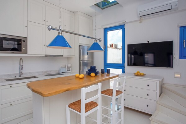 A modern kitchen with white cabinetry, a wooden island, and blue pendant lights.
