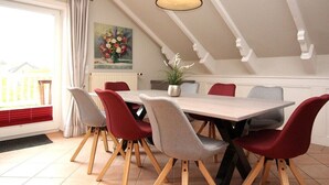 Een eetruimte met een tafel, stoelen, een potplant en een schilderij aan de muur.