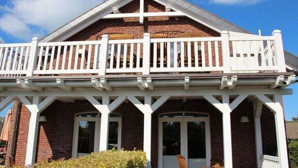 Een gebouw met twee verdiepingen, een balkon, bakstenen muren en een witte veranda.
