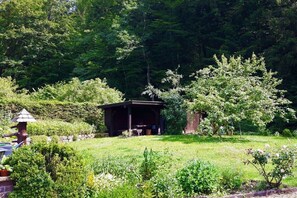Ein rustikales Holzgebäude in einer üppigen Gartenanlage mit dichter Vegetation im Hintergrund.