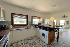 A modern kitchen with a washing machine, large windows, and a chandelier. - Holiday home in Roses with swimming pool (Roses)