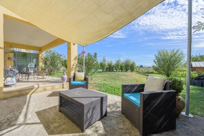 An outdoor patio with wicker furniture, a covered seating area, and a view of a grassy landscape. - Holiday Home 'Les Demeures Du Soleil - Le Ventoux' with Pool, Wi-Fi and Air Conditioning (Piolenc)