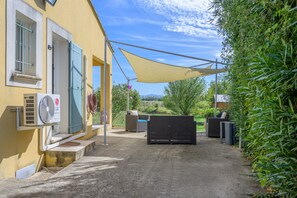 An outdoor patio area with a yellow building, a fan, outdoor furniture, and a view of the countryside. - Holiday Home 'Les Demeures Du Soleil - Le Ventoux' with Pool, Wi-Fi and Air Conditioning (Piolenc)