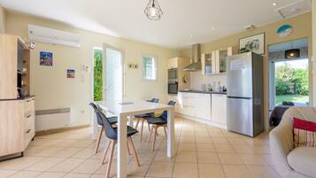 A modern kitchen with a dining area, a built-in oven, a refrigerator, and a window providing natural light.