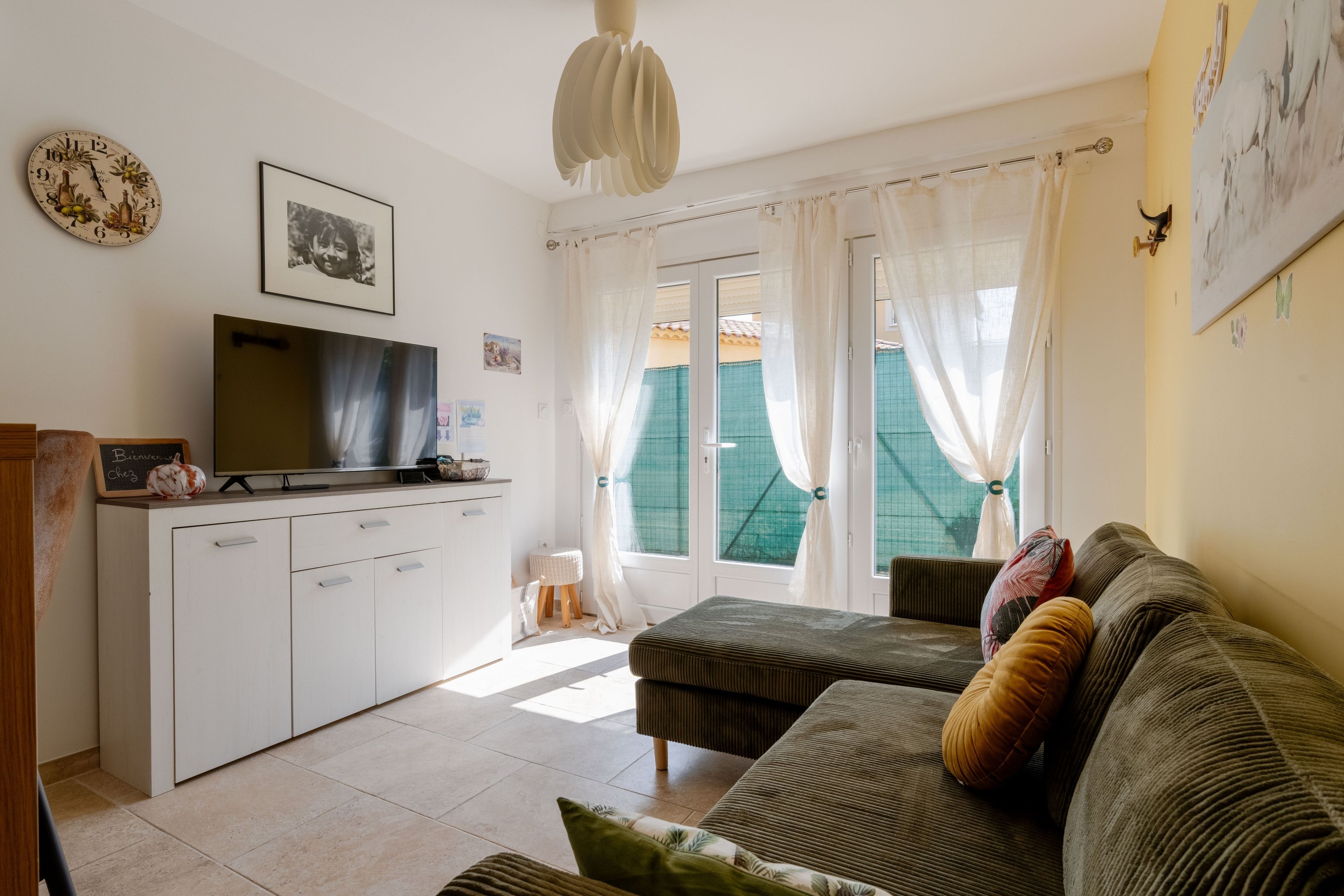 Een woonkamer met een bank, een televisie, een kast en een raam met gordijnen.