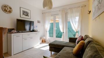 Een woonkamer met een bank, een televisie, een kast en een raam met gordijnen.