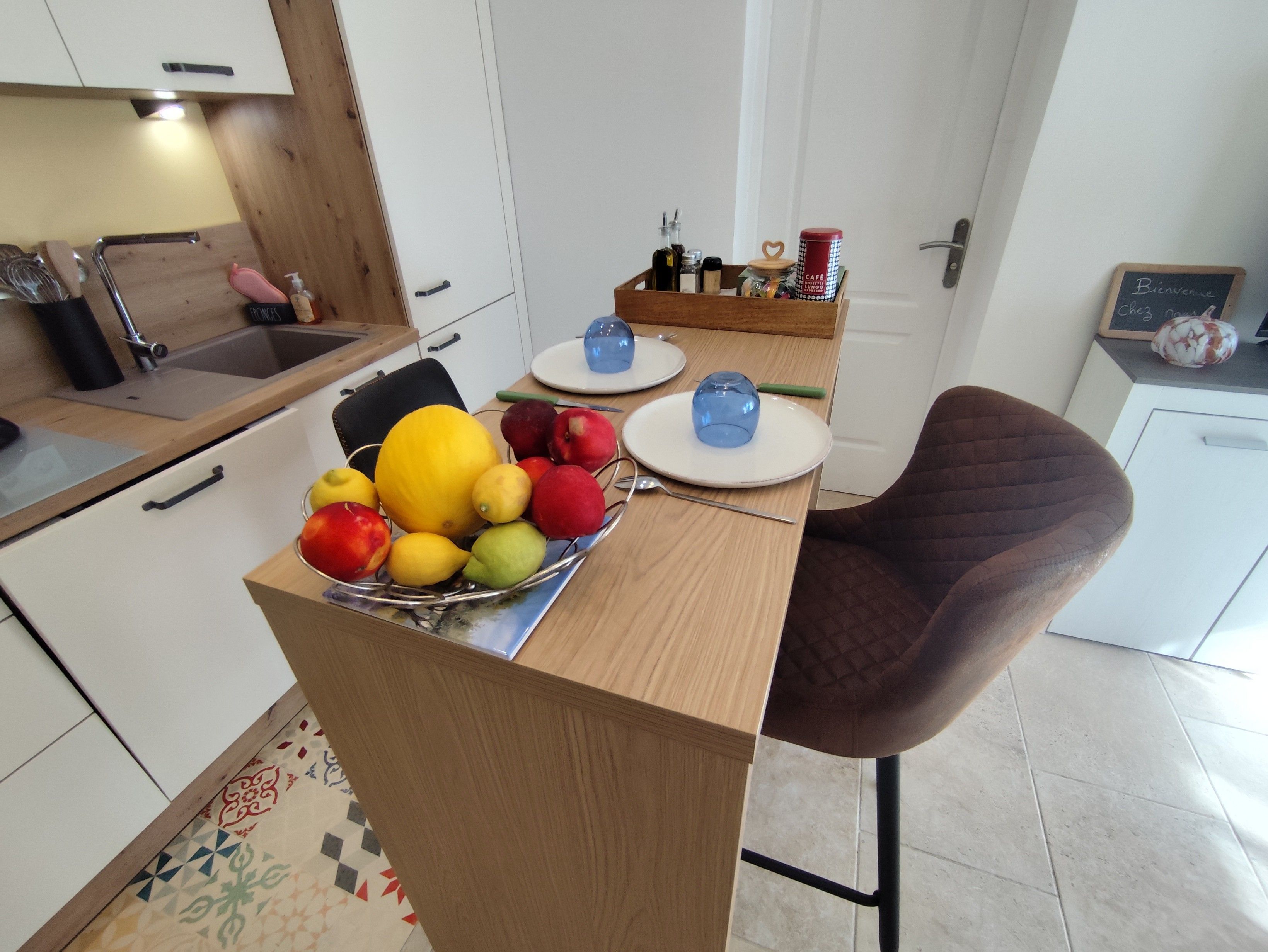 Een moderne keuken met een houten aanrecht, een eethoek met een bruine stoel en een kleine tafel met een blauw glas en een wit bord.