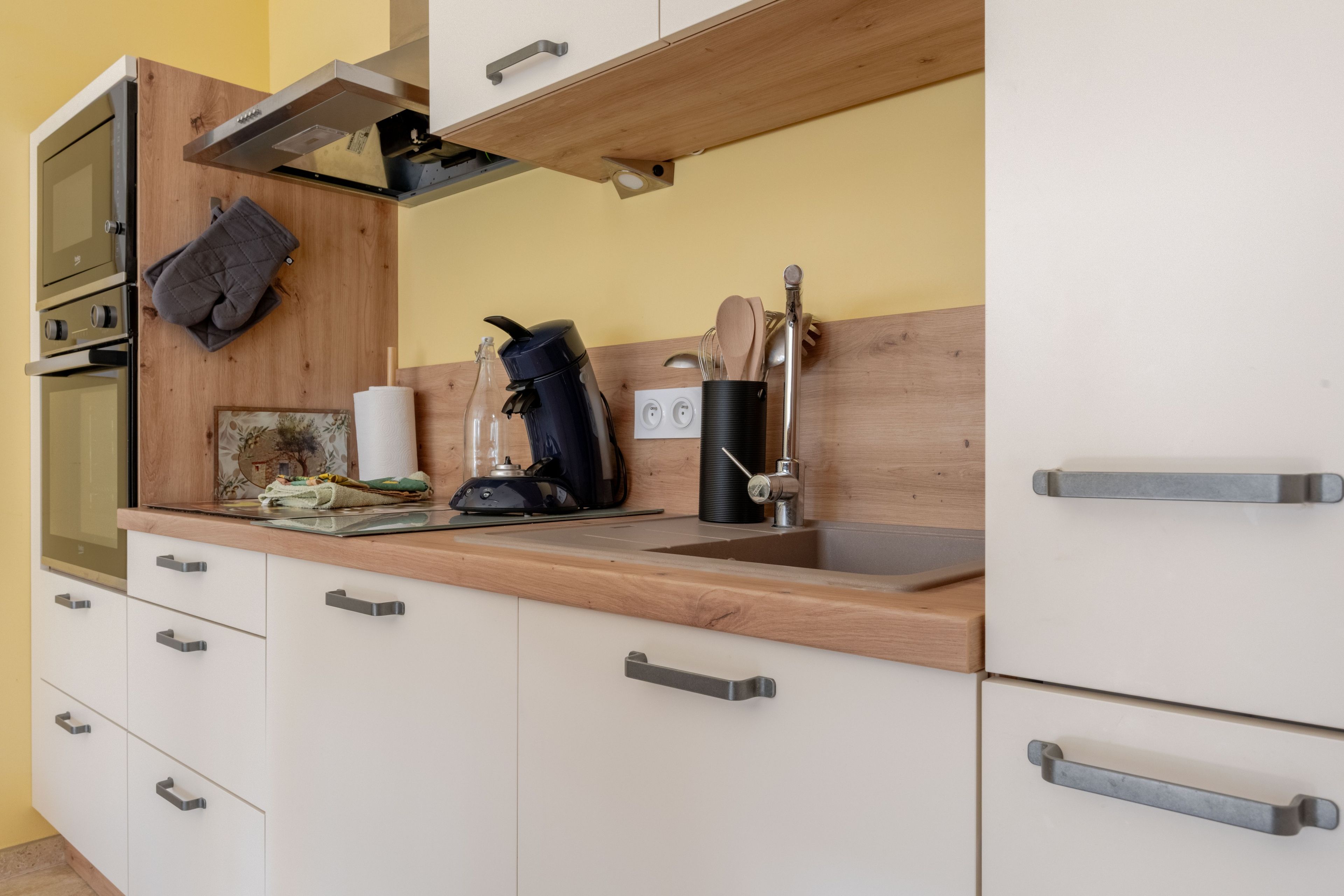 Een keuken met een houten aanrecht, een koffiezetapparaat, een waterkoker en een spoelbak.