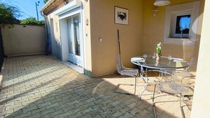 Un'area patio con un tavolo rotondo in vetro e sedie, una piccola finestra e una porta che dà all'interno.