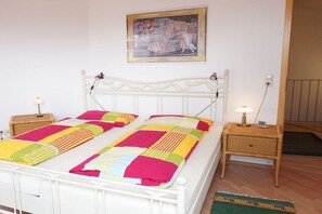 A bed with a colorful quilt, a white headboard, two bedside tables with lamps, and a painting on the wall. - Holiday apartment with 3 bedrooms (Meersburg)
