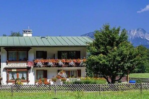 A two-story building with a balcony, surrounded by greenery and mountains in the background. - Holiday apartment with 1 bedroom (Schönau am Königssee)