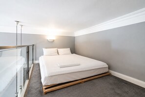 Et sovev ærelse med en seng, et sengebord, en lampe og en glasvæg.