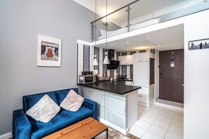En moderne lejlighed med en blå sofa, et køkken med mikrobølgeovn og et bybillede på væggen.