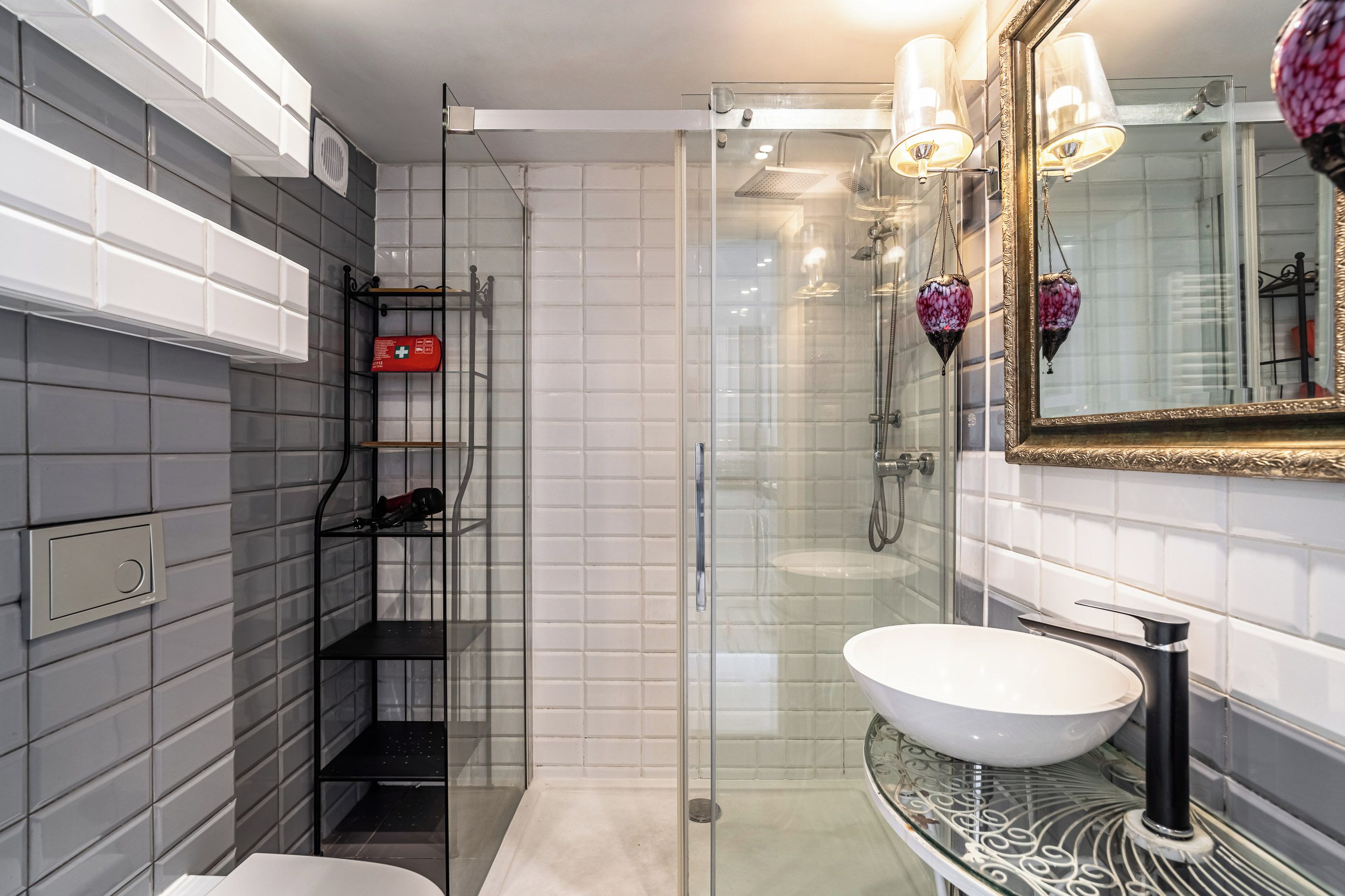 A modern bathroom with a glass-enclosed shower, a white sink, and a mirror with a decorative frame.