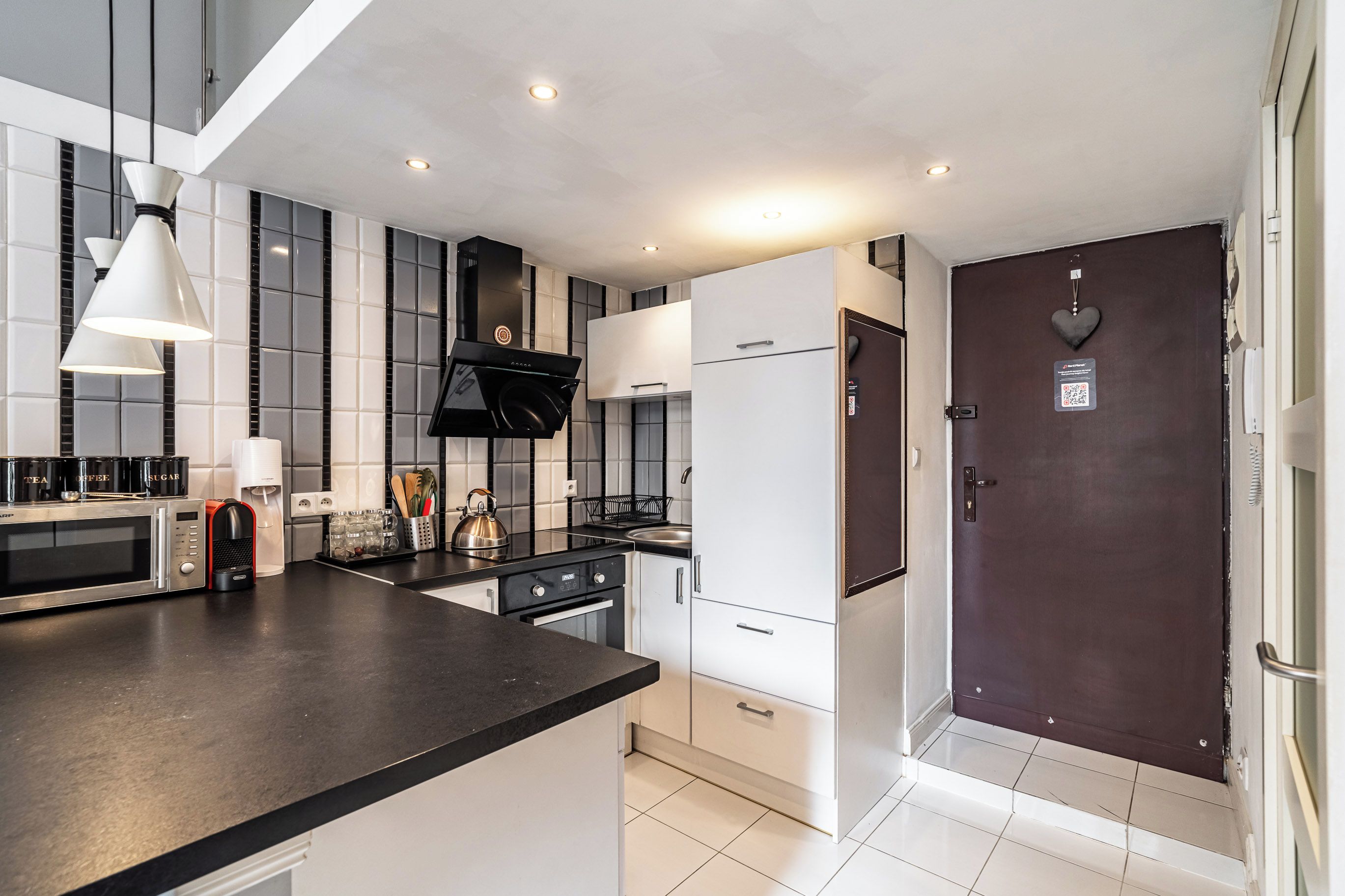 A modern kitchen with a black countertop, stainless steel appliances, and a dark wooden door.
