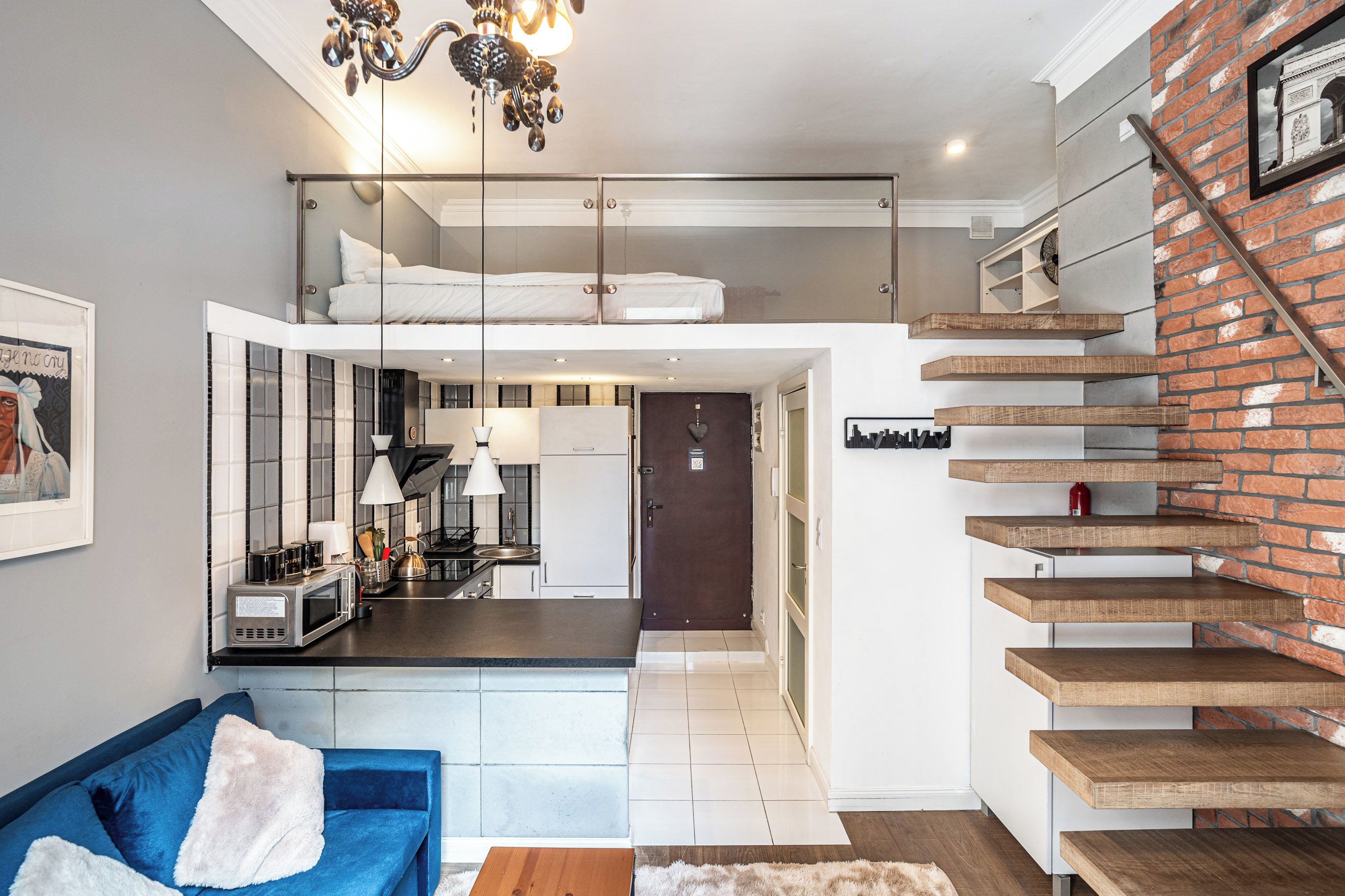 A modern apartment with a kitchen, dining area, and a staircase with exposed brick walls.