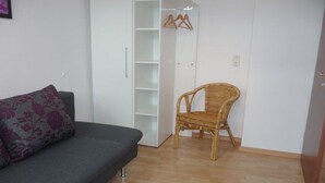 A room with a grey sofa, a wicker chair, and a white wardrobe with hanging space. - Holiday apartment with 2 bedrooms (Traben-Trarbach\/Wolf)
