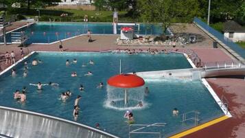 En stor udendørs swimmingpool med flere baner, et vandrutsjebane og et redningstårn.