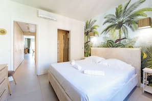 A hotel room with a bed, a headboard with a tropical mural, a bedside table, and an air conditioning unit. - Apartment in Cannes with 2 bedrooms sleeps 4 (Cannes)