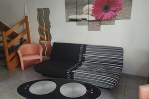 A room with a black and white striped sofa, a pink chair, and a black table with two white circular objects. - Holiday home with 2 bedrooms (Narbonne-Plage)