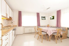 A kitchen with wooden cabinets, a dining table with chairs, and a bench. - House Alpenglühn || Ofterschwang (Ofterschwang)