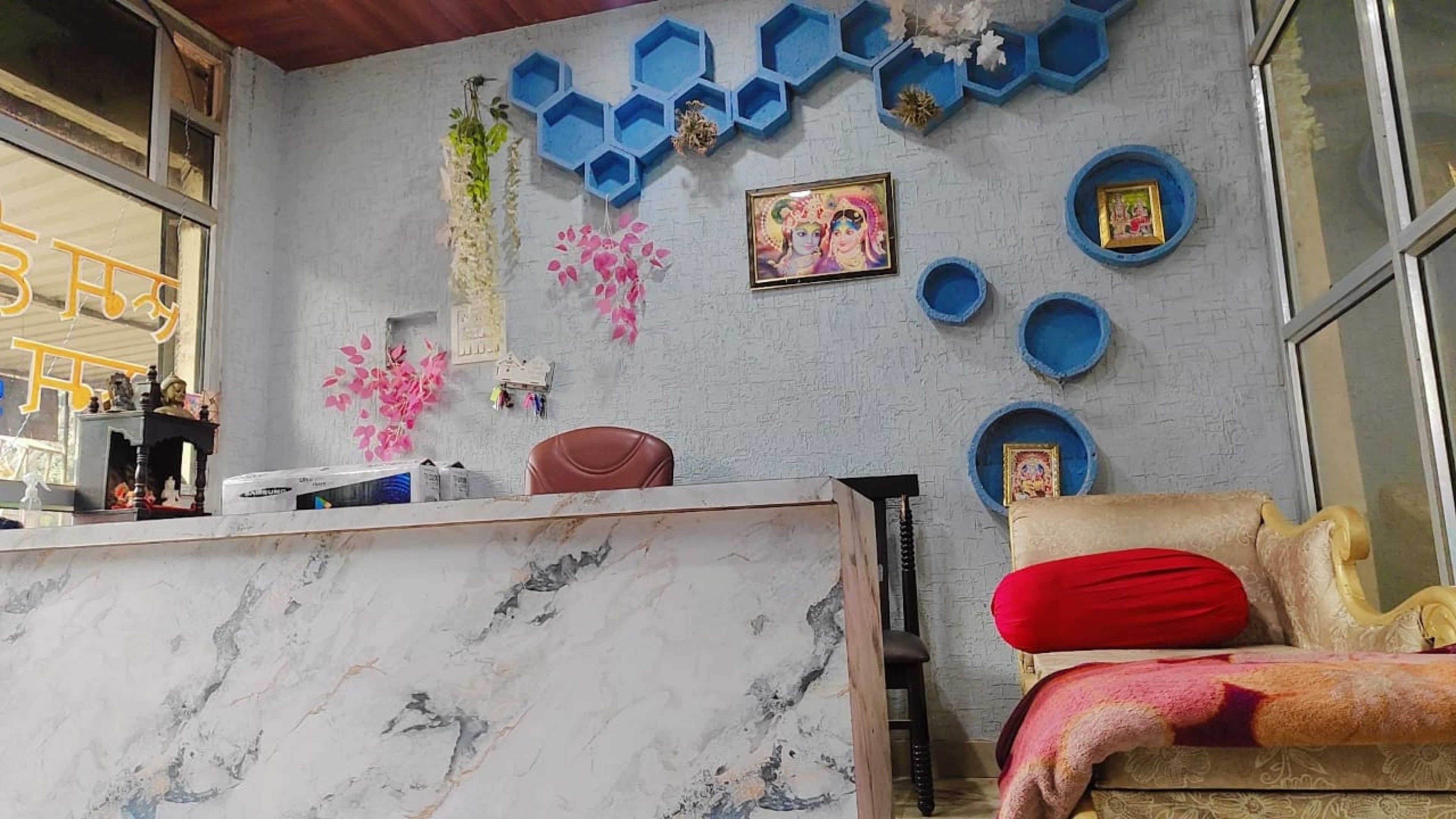 Una habitación con un mostrador de recepción de mármol, un sofá con un cojín rojo y una pared decorada con estantes azules hexagonales y cuadros enmarcados.