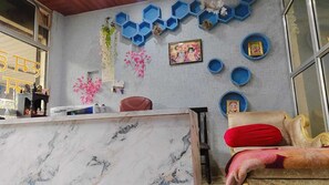 Una habitación con un mostrador de recepción de mármol, un sofá con un cojín rojo y una pared decorada con estantes azules hexagonales y cuadros enmarcados.