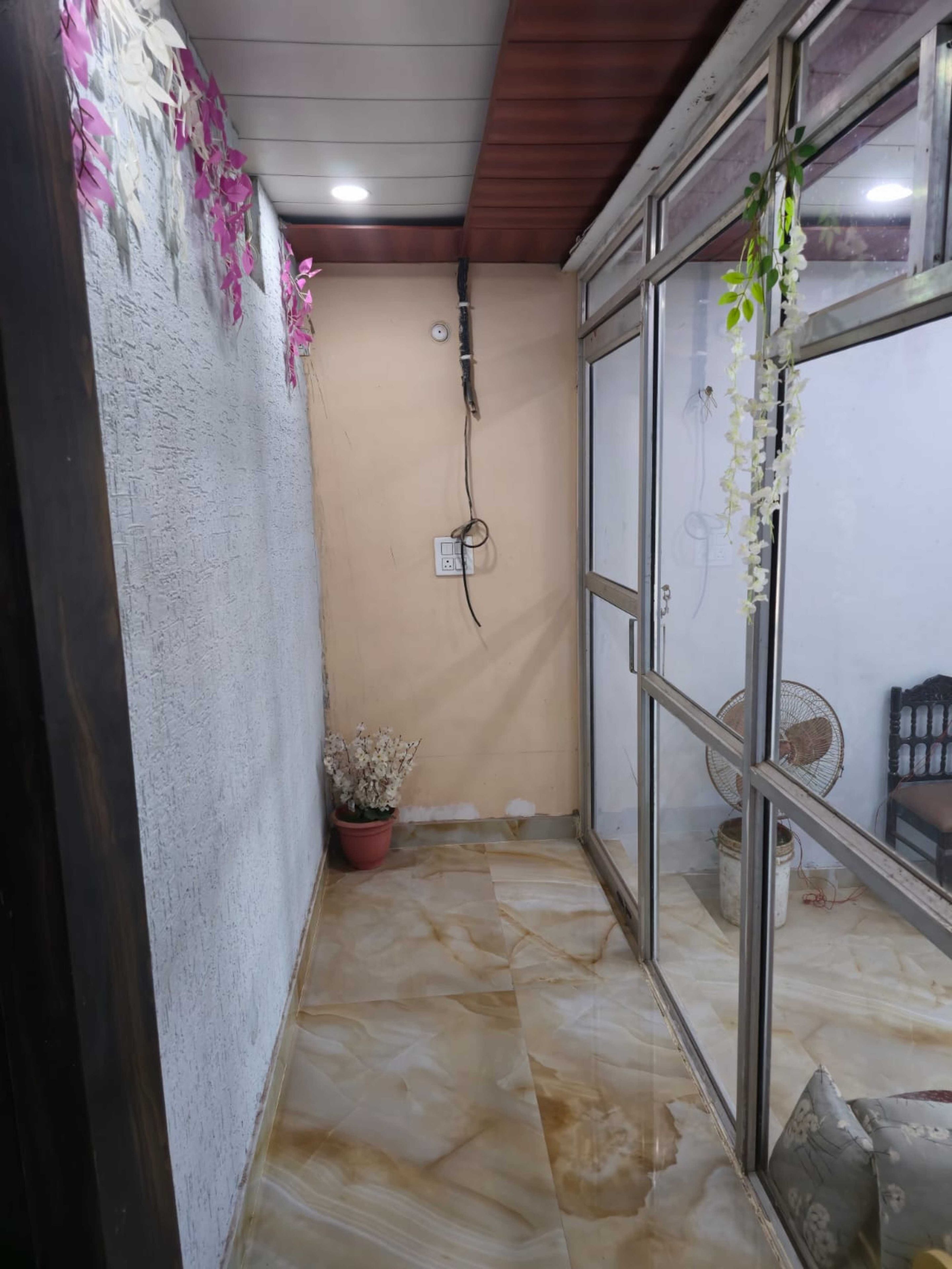 Un pasillo estrecho con una planta en maceta, un ventilador de techo y una ventana con vistas al exterior.