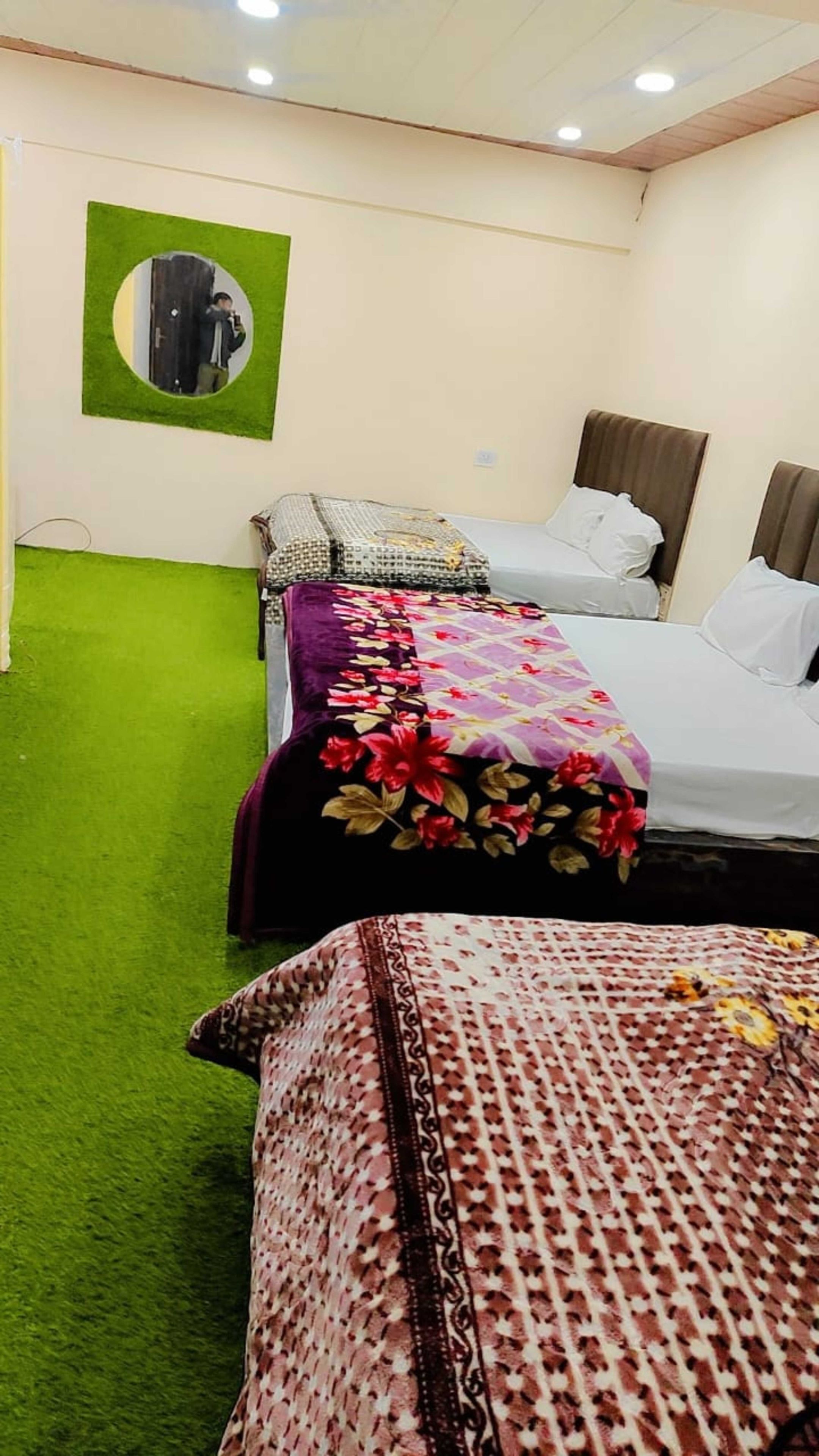 Habitación de hotel con dos camas, alfombra verde y espejo circular montado en la pared.