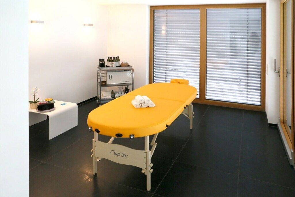 A treatment room with a massage table, a small table with bottles, and a bench.