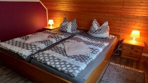 A double bed with patterned bedding and pillows, wooden walls, and bedside lamps. - Holiday apartment with 3 bedrooms (Olsberg-Elpe)
