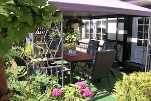 Une terrasse extérieure avec une table et des chaises, entourée de verdure et de plantes.