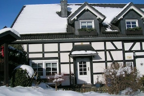 Une maison traditionnelle à colombages, avec un toit enneigé et une porte blanche.