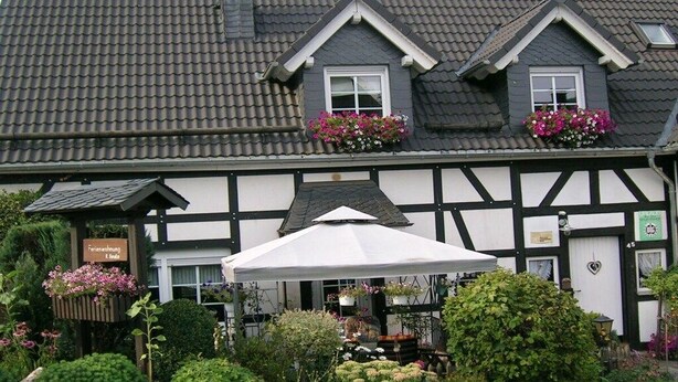 A traditional half-timbered building with a tiled roof, flower boxes on the upper windows, and a white umbrella in front. - Holiday apartment with 3 bedrooms (Olsberg-Elpe)