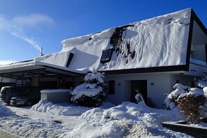 A house covered in snow with a garage and a car parked in front. - Holiday apartment with 1 bedroom (Titisee-Neustadt)
