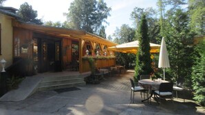 An outdoor patio area with wooden tables and chairs, umbrellas, and a building with a wooden facade. - B 2 Directly at Lake Netzen (Kloster Lehnin)