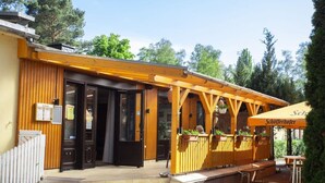A wooden building with a covered patio area, outdoor seating, and a sign indicating a restaurant. - B 2 Directly at Lake Netzen (Kloster Lehnin)