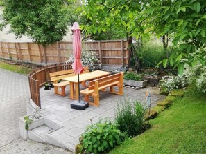 An outdoor patio with a wooden table and benches, surrounded by a wooden fence and greenery. - 3 - Schuepferlingshof (Kunreuth)
