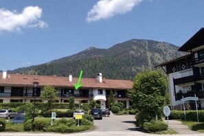 A hotel with a red-tiled roof, a parking area, and a mountain backdrop. - Holiday apartment with 2 bedrooms (Walchensee)