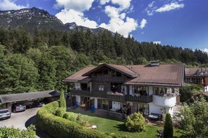 A two-story chalet with a balcony, surrounded by lush greenery and mountains. - 1 - On the Loisach || Garmisch-Partenkirchen (Garmisch-Partenkirchen)