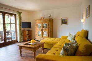 A living room with a yellow sofa, a wooden coffee table, and a cabinet with decorative doors. - 1 - On the Loisach || Garmisch-Partenkirchen (Garmisch-Partenkirchen)