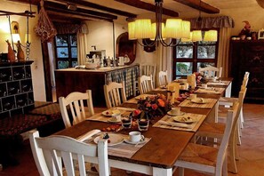 Ein Essbereich mit einem langen Holztisch, gedeckt für eine Mahlzeit, umgeben von weißen Stühlen, mit einer Bar und Regalen im Hintergrund.