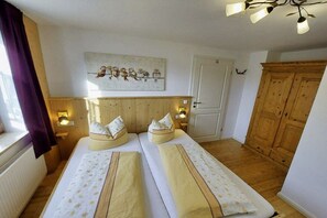 Ein Schlafzimmer mit zwei Betten, einem Holzschrank, einem Bild an der Wand und einem Fenster mit Vorhängen.
