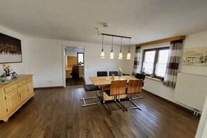 Ein Essbereich mit Holztisch und -stühlen, Pendelleuchten und Blick ins Freie durch ein fensterbepflanztes Fenster.