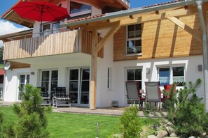 A two-story building with a balcony, large windows, and outdoor seating. - Holiday apartment with 1 bedroom (Fischen)