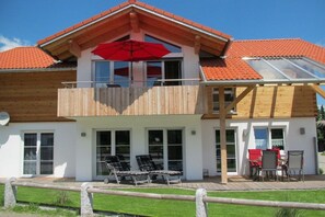 A two-story house with a balcony, a red umbrella, and a patio area with chairs and a table. - Holiday apartment with 1 bedroom (Fischen)