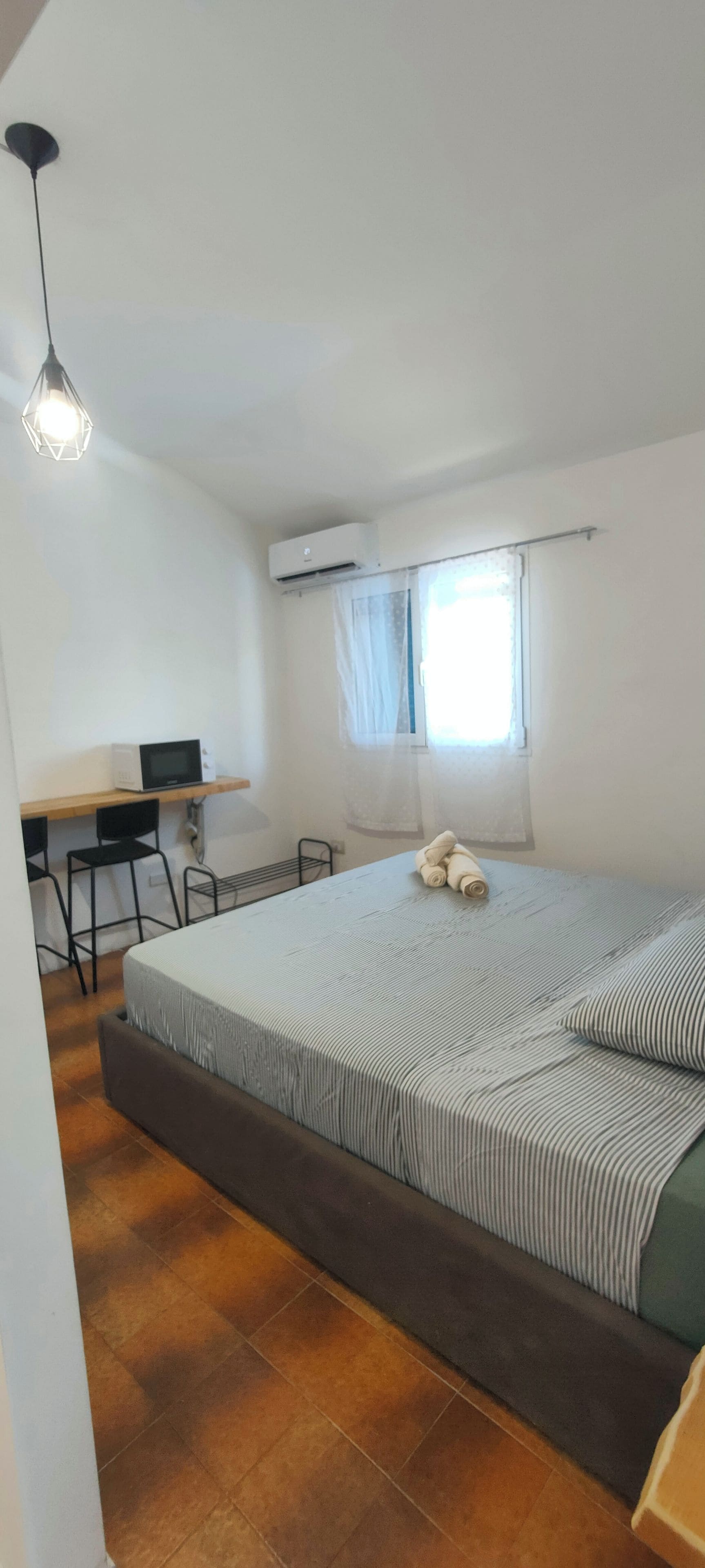 Ein Schlafzimmer mit Bett, Schreibtisch, Stuhl, Klimaanlage und einem Fenster mit Vorhängen.