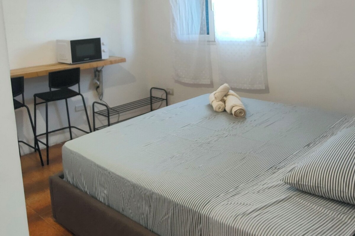 A bedroom with a bed, a desk, a chair, an air conditioner, and a window with curtains.