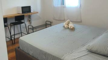 Ein Schlafzimmer mit Bett, Schreibtisch, Stuhl, Klimaanlage und einem Fenster mit Vorhängen.