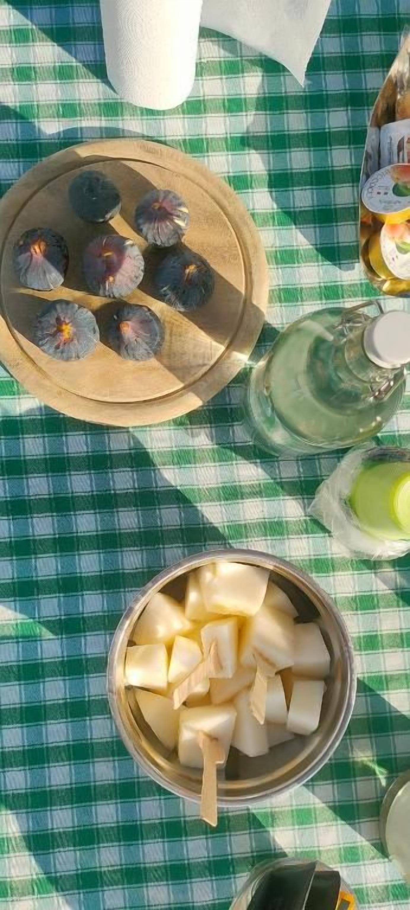 Una mesa con mantel a cuadros, un plato de madera con alimentos, un bol de metal con cubos y una botella de líquido.